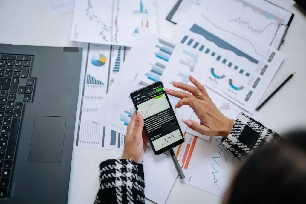 Pebisnis menganalisis data keuangan di smartphone dengan laptop dan dokumen
